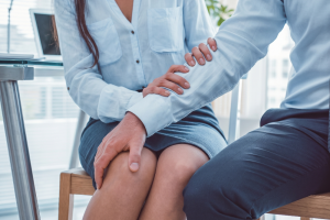 Healthcare professional in a light blue blouse holds a patient’s forearm during a consultation in a bright clinic setting.